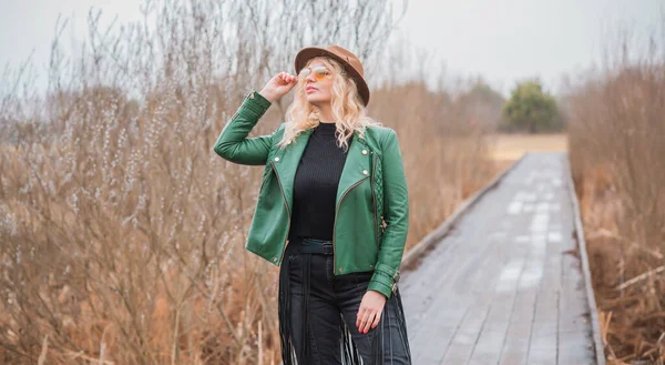 Kadın, eko-deri yeşil ceket, Fedora kahverengi şapka ve eski model havacı gözlükleri giyiyor, püsküllü kemer, moda konsept. 