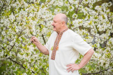 Çiçek bahçesinde nakışlı gömlekli yaşlı adam.