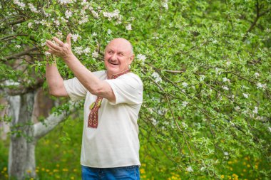 Çiçek bahçesinde nakışlı gömlekli yaşlı adam.