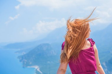 Tatil ve yaz konsepti. Kızıl saçlı kız güneşli bir günde sıcak havanın ve manzaranın tadını çıkarıyor. Bayramlarda bordo elbiseli kadın
