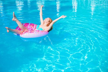 Sıcak ve güneşli bir günde havuzda donut yiyen bir kadın. Yaz tatili cennet gibi. Havuzdaki şişme yatakta bikinili kadın güneşleniyor..