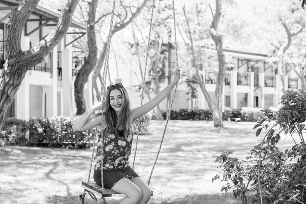 Happy moments of life. Vacation concept. Happy young woman at good mood sitting on swing enjoying garden view.