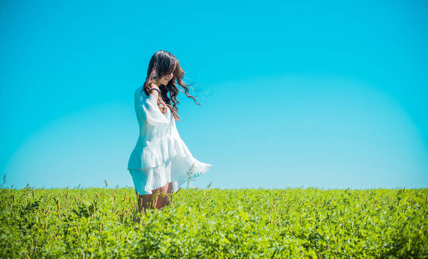Freedom concept. Young happy woman in green field, evening light. Blue sky behind. Beauty Girl Outdoors enjoying nature. Beautiful Teenage Model girl in white dress running on the meadow