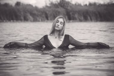 Suyun içinde siyah elbiseli seksi mistik kadın. Kadınlık ve şehvet kavramı. Rahat ol. Şık vücutlu bir kadın doğada dinleniyor, çekici kızıl saçlı bayan hayatın tadını çıkarıyor.