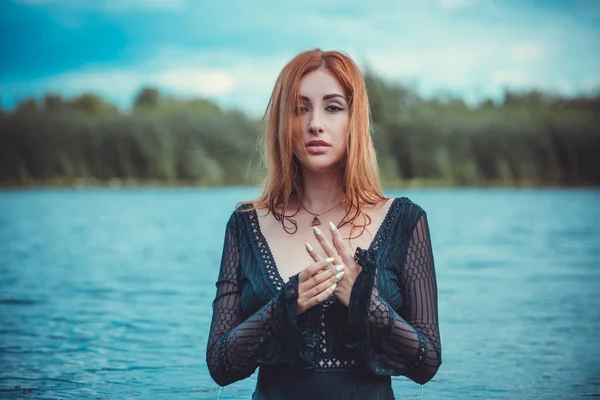 Sexy mystical woman in black bodysuit in water. Concept of femininity and sensual. Relax concept. Woman with fashionable figure rest at nature, attractive redhead lady enjoy the life