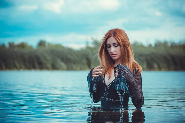 Sexy mystical woman in black bodysuit in water. Concept of femininity and sensual. Relax concept. Woman with fashionable figure rest at nature, attractive redhead lady enjoy the life