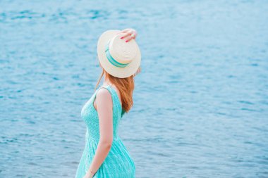 Modaya uygun ve romantik kadınlar gibi. Plajda turkuaz elbiseli hasır şapkalı bir kız.