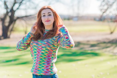 Güzel, gülümseyen kızıl saçlı, bahar günü neşeli, sıradan bir tarzı olan, yün mavi ceketli ve renkli kazaklı bir kız.