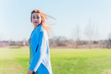 Güzel, gülümseyen kızıl saçlı, bahar günü neşeli, sıradan bir tarzı olan, yün mavi ceketli ve renkli kazaklı bir kız.