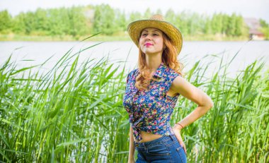 Sazlıkta gülümseyen saman şapkalı olumlu bir genç kadın, klasik tarzda, nehir veya gölde dinleniyor. Amerikan tarzı