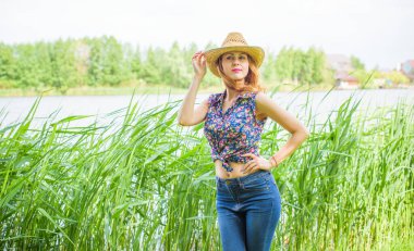 Sazlıkta gülümseyen saman şapkalı olumlu bir genç kadın, klasik tarzda, nehir veya gölde dinleniyor. Amerikan tarzı