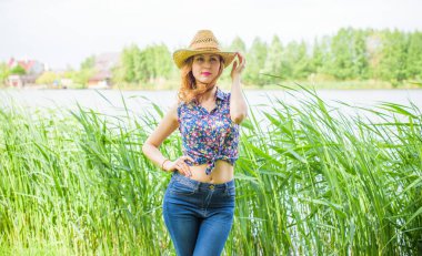 Sazlıkta gülümseyen saman şapkalı olumlu bir genç kadın, klasik tarzda, nehir veya gölde dinleniyor. Amerikan tarzı