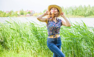 Sazlıkta gülümseyen saman şapkalı olumlu bir genç kadın, klasik tarzda, nehir veya gölde dinleniyor. Amerikan tarzı