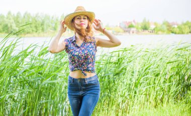 Sazlıkta gülümseyen saman şapkalı olumlu bir genç kadın, klasik tarzda, nehir veya gölde dinleniyor. Amerikan tarzı