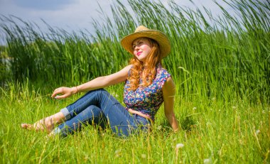 Sazlıkta gülümseyen saman şapkalı olumlu bir genç kadın, klasik tarzda, nehir veya gölde dinleniyor. Amerikan tarzı