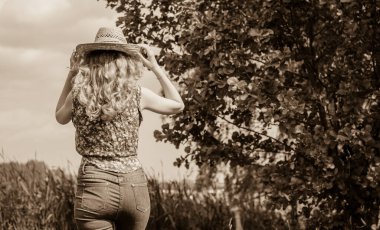 Sazlıkta gülümseyen saman şapkalı olumlu bir genç kadın, klasik tarzda, nehir veya gölde dinleniyor. Amerikan tarzı