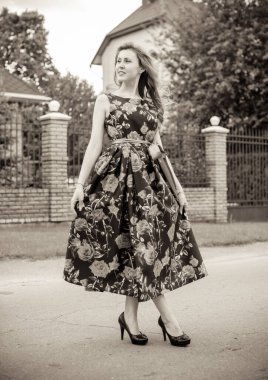 Yazın arka planında gül desenli kırmızı dudaklı, kırmızı elbiseli bir Retro Girl. Bir gül dalının arka planında genç bir kızıl manken. Şık bir kadın. Şık bir yaz elbisesi.