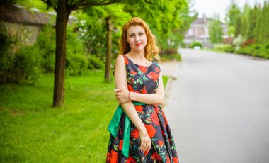 Yazın arka planında gül desenli kırmızı dudaklı, kırmızı elbiseli bir Retro Girl. Bir gül dalının arka planında genç bir kızıl manken. Şık bir kadın. Şık bir yaz elbisesi.