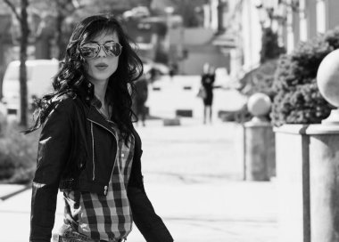 Güzel ve şık esmer kadın güneşli bir günde şehirde yürüyor, modern gündelik tarzda.