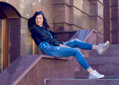 Güzel ve şık esmer kadın güneşli bir günde şehirde yürüyor, modern gündelik tarzda.