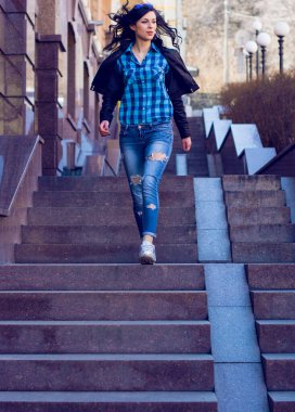 Güzel ve şık esmer kadın güneşli bir günde şehirde yürüyor, modern gündelik tarzda.