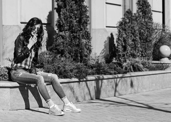 街でタバコを吸う青いシャツとジーンズのブルネットの女性 — ストック写真