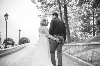 Bahçede çiçeklerin arasında, uzun, açık renk bir elbiseyle muhteşem şekilleri olan güzel sarışın gelin. Gelin ve damat yolda.