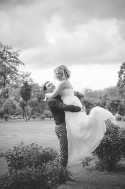 Bahçede çiçeklerin arasında, uzun, açık renk bir elbiseyle muhteşem şekilleri olan güzel sarışın gelin. Gelin ve damat yolda.