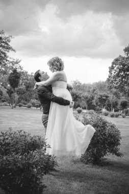 Bahçede çiçeklerin arasında, uzun, açık renk bir elbiseyle muhteşem şekilleri olan güzel sarışın gelin. Gelin ve damat yolda.