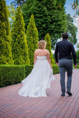 Bahçede çiçeklerin arasında, uzun, açık renk bir elbiseyle muhteşem şekilleri olan güzel sarışın gelin. Gelin ve damat yolda.