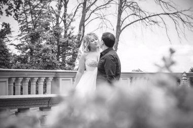 Bahçede çiçeklerin arasında, uzun, açık renk bir elbiseyle muhteşem şekilleri olan güzel sarışın gelin. Gelin ve damat yolda.