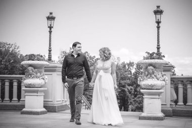 Bahçede çiçeklerin arasında, uzun, açık renk bir elbiseyle muhteşem şekilleri olan güzel sarışın gelin. Gelin ve damat yolda.