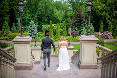 Bahçede çiçeklerin arasında, uzun, açık renk bir elbiseyle muhteşem şekilleri olan güzel sarışın gelin. Gelin ve damat yolda.