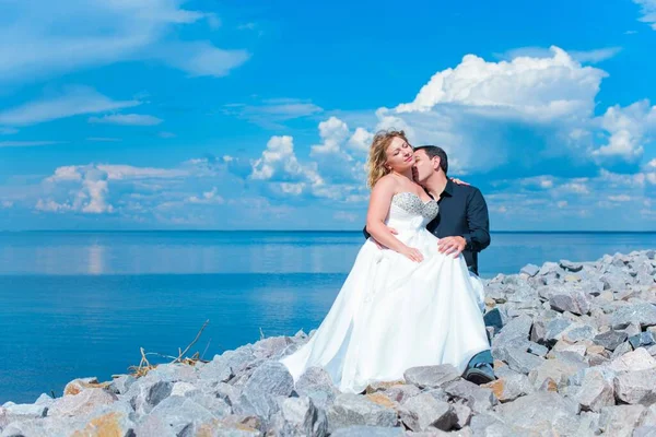 Bahçede çiçeklerin arasında, uzun, açık renk bir elbiseyle muhteşem şekilleri olan güzel sarışın gelin. Gelin ve damat yolda.