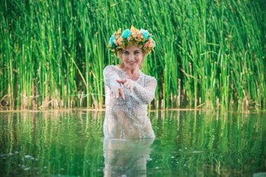 Uzun, beyaz dantelli bir elbise ve çelenk giymiş muhteşem bir göl perisi. Sanatsal fotoğrafçılık, gizemli sahne. Avrupalı cadı. Peri masalı