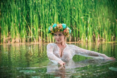 Uzun, beyaz dantelli bir elbise ve çelenk giymiş muhteşem bir göl perisi. Sanatsal fotoğrafçılık, gizemli sahne. Avrupalı cadı. Peri masalı