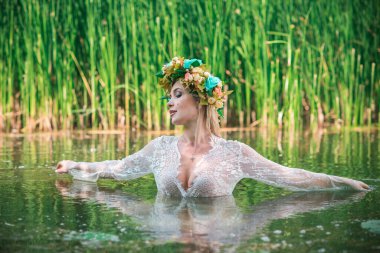 Uzun, beyaz dantelli bir elbise ve çelenk giymiş muhteşem bir göl perisi. Sanatsal fotoğrafçılık, gizemli sahne. Avrupalı cadı. Peri masalı