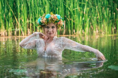 Uzun, beyaz dantelli bir elbise ve çelenk giymiş muhteşem bir göl perisi. Sanatsal fotoğrafçılık, gizemli sahne. Avrupalı cadı. Peri masalı