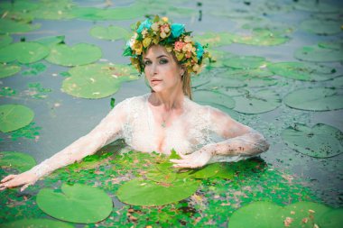 Uzun, beyaz dantelli bir elbise ve çelenk giymiş muhteşem bir göl perisi. Sanatsal fotoğrafçılık, gizemli sahne. Avrupalı cadı. Peri masalı