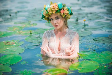 Uzun, beyaz dantelli bir elbise ve çelenk giymiş muhteşem bir göl perisi. Sanatsal fotoğrafçılık, gizemli sahne. Avrupalı cadı. Peri masalı