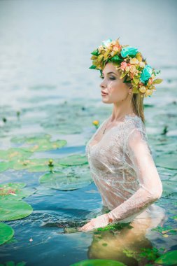 Uzun, beyaz dantelli bir elbise ve çelenk giymiş muhteşem bir göl perisi. Sanatsal fotoğrafçılık, gizemli sahne. Avrupalı cadı. Peri masalı