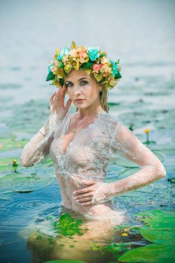 Uzun, beyaz dantelli bir elbise ve çelenk giymiş muhteşem bir göl perisi. Sanatsal fotoğrafçılık, gizemli sahne. Avrupalı cadı. Peri masalı