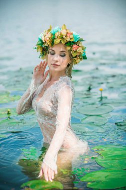 Uzun, beyaz dantelli bir elbise ve çelenk giymiş muhteşem bir göl perisi. Sanatsal fotoğrafçılık, gizemli sahne. Avrupalı cadı. Peri masalı