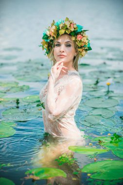 Uzun, beyaz dantelli bir elbise ve çelenk giymiş muhteşem bir göl perisi. Sanatsal fotoğrafçılık, gizemli sahne. Avrupalı cadı. Peri masalı