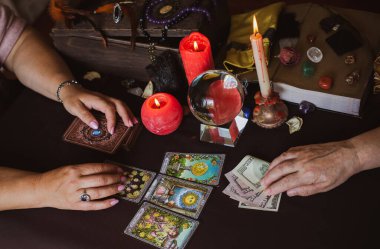 Seance of magic wish a money, fortune telling on a Tarot cards, candles and fortune-telling objects. The concept of divination, astrology and esotericism - illustrative editorial - Romania- Transylvania 9 May clipart