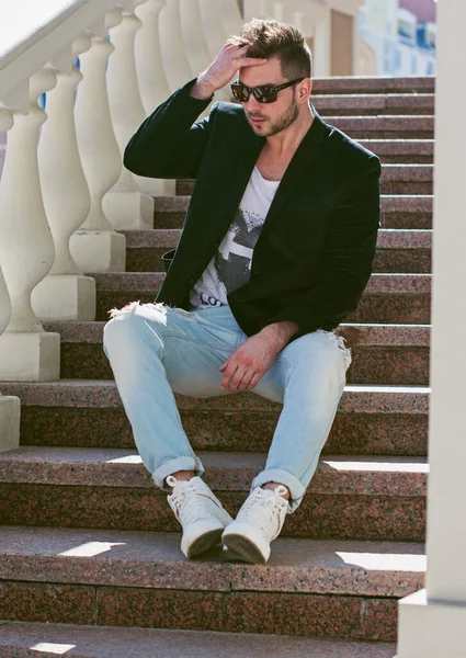 Yakışıklı genç adam eski kentte mavi kot, siyah ceket, beyaz gömlek, gözlük, şık saç, iyi ruh hali, güzel moda erkek arkadaş, vatandaş, güzel yüze sahip.