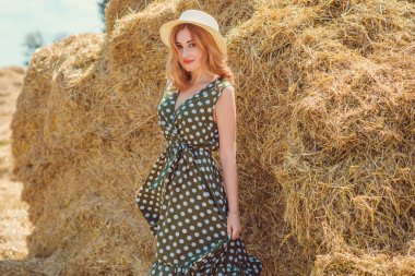 Country tarzı bir karışım, güzel kızıl saçlı bir kadın. Samanlıkta güzel bir bayanın portresi. Yeşil benekli elbiseli ve şapkalı kadın. Moda konsepti