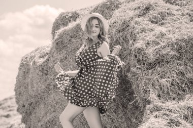 Country tarzı bir karışım, güzel kızıl saçlı bir kadın. Samanlıkta güzel bir bayanın portresi. Yeşil benekli elbiseli ve şapkalı kadın. Moda konsepti