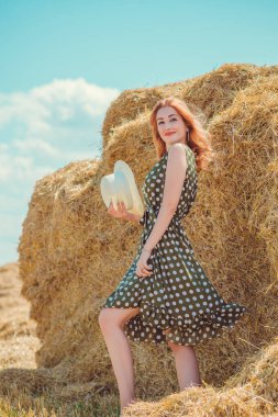 Country tarzı bir karışım, güzel kızıl saçlı bir kadın. Samanlıkta güzel bir bayanın portresi. Yeşil benekli elbiseli ve şapkalı kadın. Moda konsepti