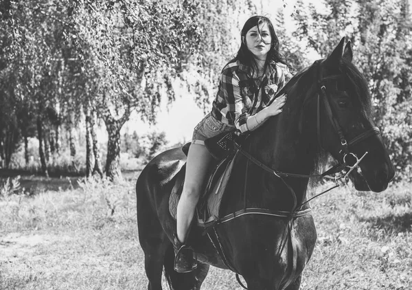Woman enjoying horse company. Young Beautiful Woman dressed plaid shirt With black Horse Outdoors, stylish girl at American country style
